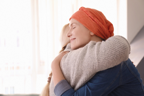 Picture of an elderly woman leaned in hugging another woman. They are both smiling.