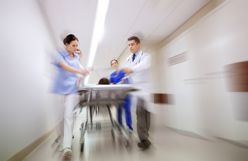 Picture of four Medical Staff pushing a patient down a hall on a stretcher in motion. There is two females and two males.