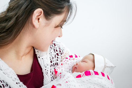 Picture of a mother holding her newborn baby while she sleeps. The mother is looking down and smiling at the baby.