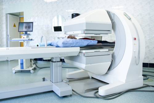 Picture of a Nuclear Medicine imaging Scanner. There is a male patient lying flat on his back using a pillow for support under his head.