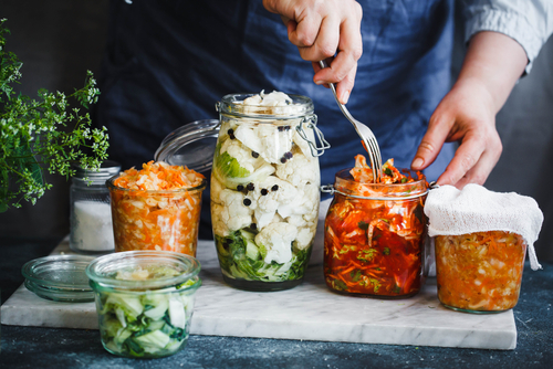 Picture of a person wearing an apron and using a fork to push food into five glass containers.