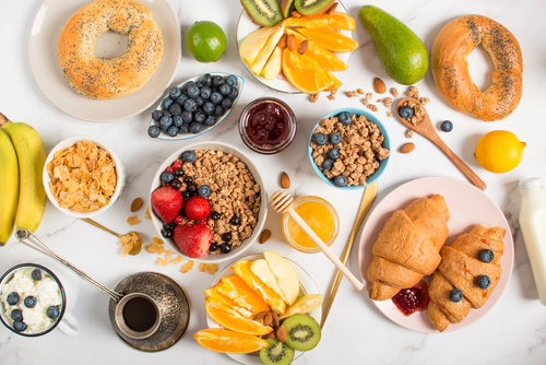 Picture of a healthy breakfast of fruits, bagels, grains, crescent rolls with fruit, and a cup of tea.